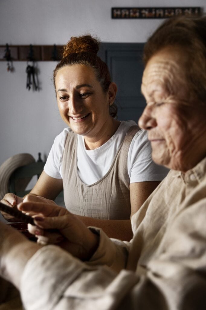 Caregiver helping an elderly woman use her phone at the kitchen table