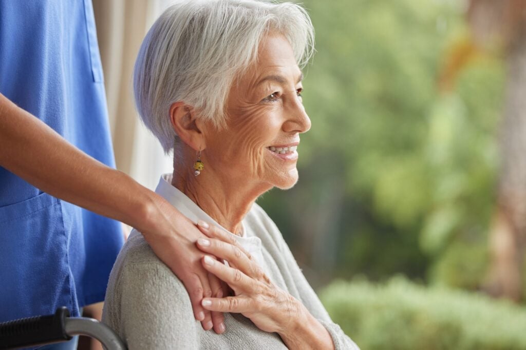 Nurse care manager resting a reassuring hand on the shoulder of a smiling senior woman